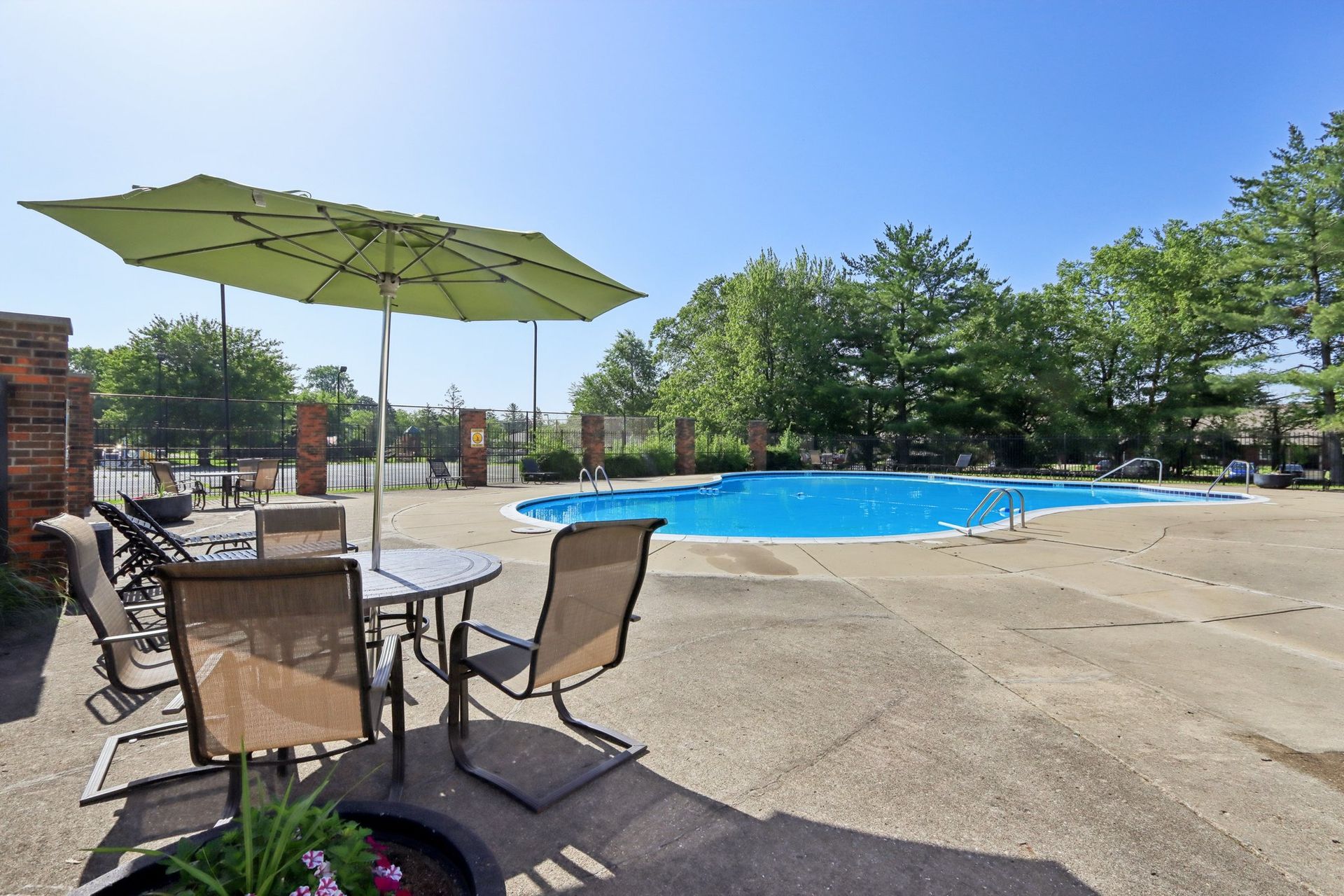 A pool area with patio furniture, a green umbrella, and blue water on a sunny day.