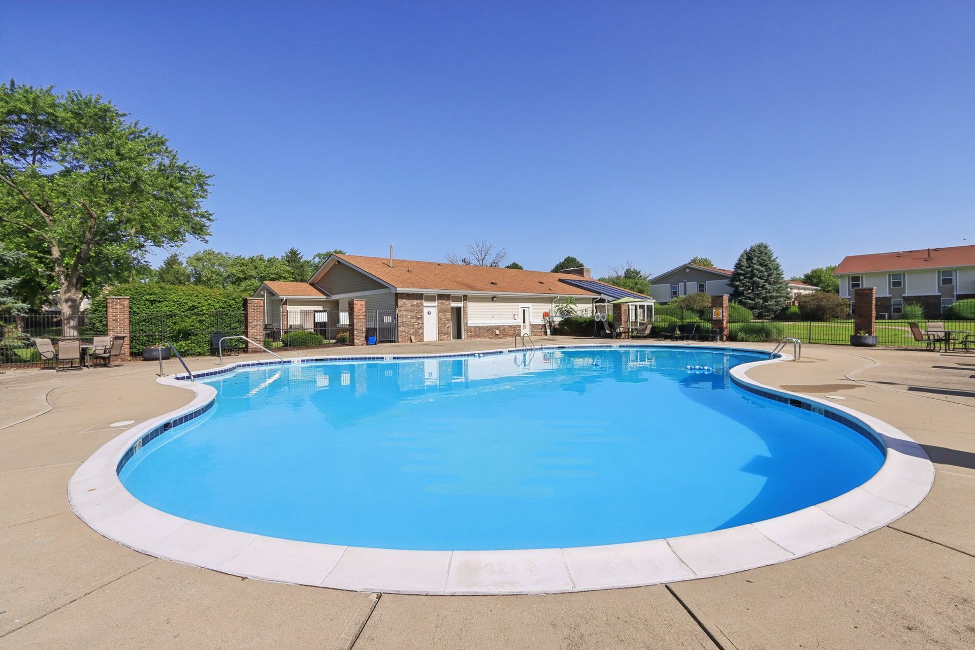 Swimming pool on a sunny day, surrounded by concrete and a small building.