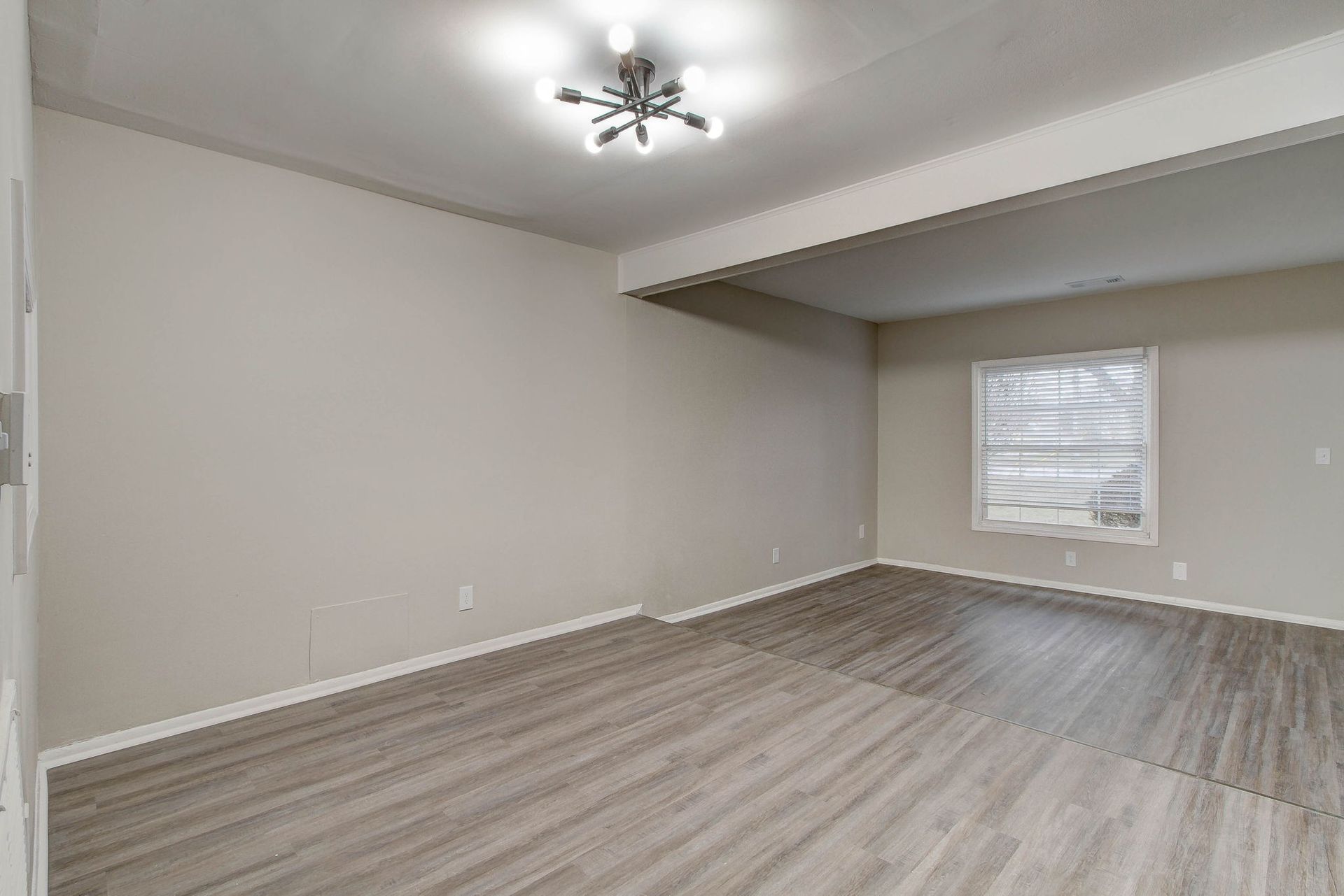 Empty room with gray walls, wood-look flooring, window, and ceiling light.