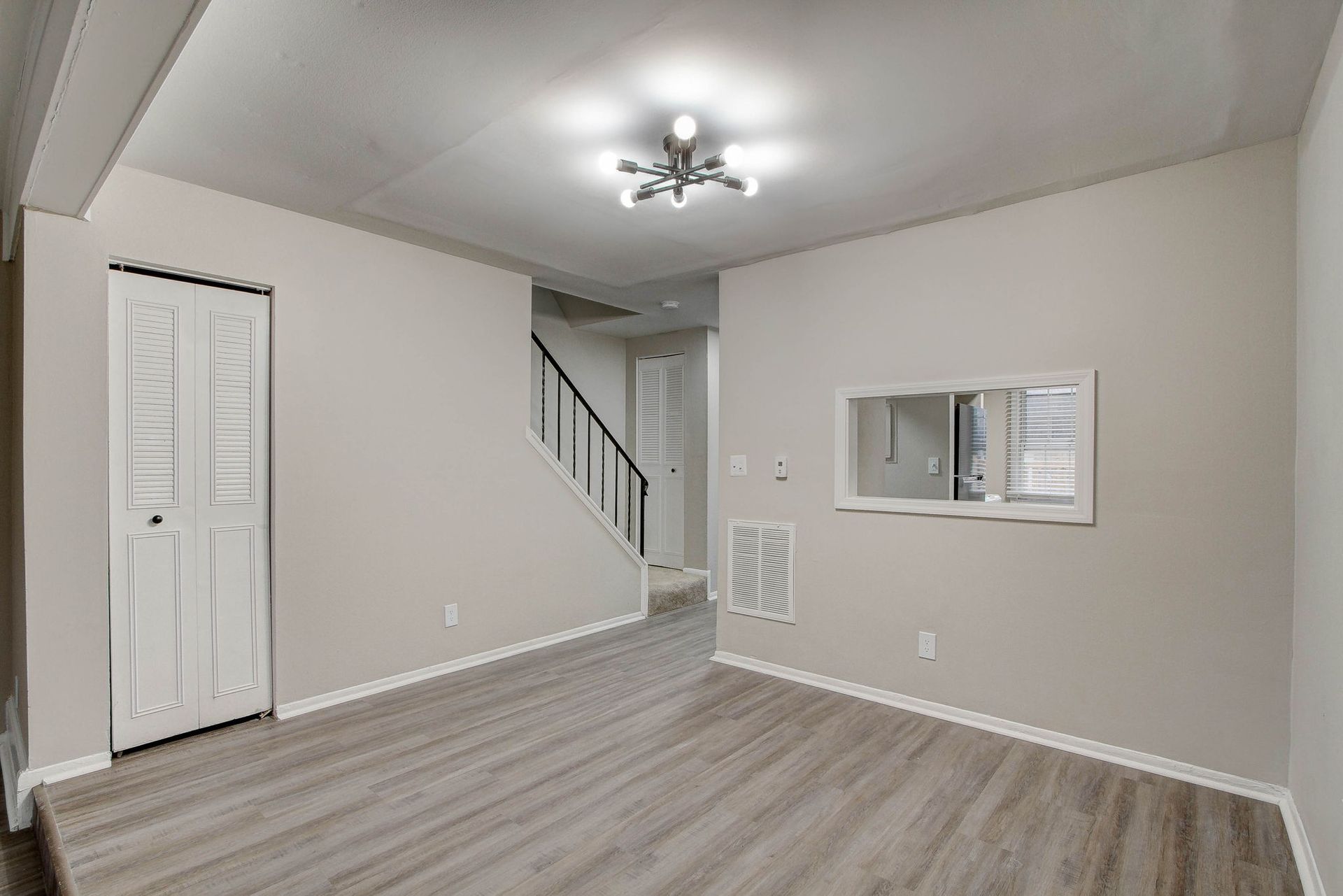 Interior view of living space with stairs and a mirror. Gray walls and light wood floors.