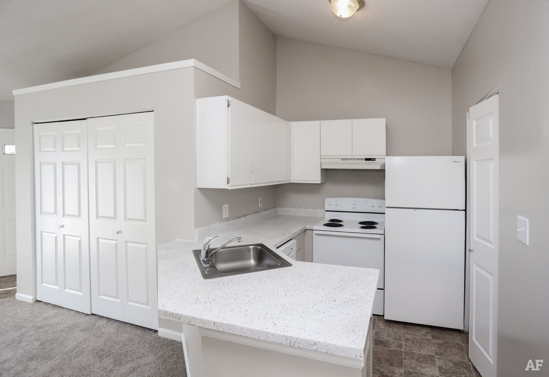 White kitchen with white appliances and cabinets, light countertop, and gray walls.