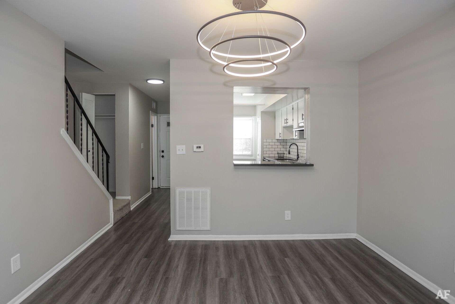 Dining room with gray walls, wood-look floor, open kitchen pass-through, stairs to the left, modern chandelier.