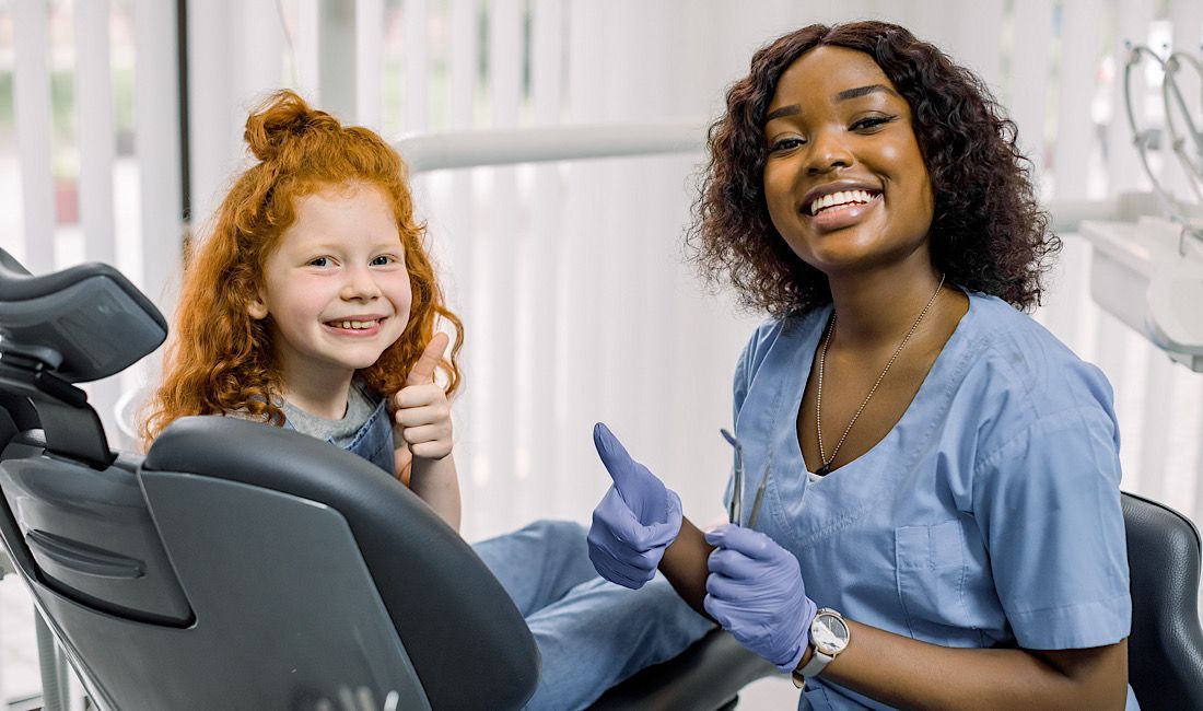 Child and dental hygienist smiling with thumbs up in a dental chair. Positive and happy visit for a child at a pediatric routine check-up in Salinas, CA.