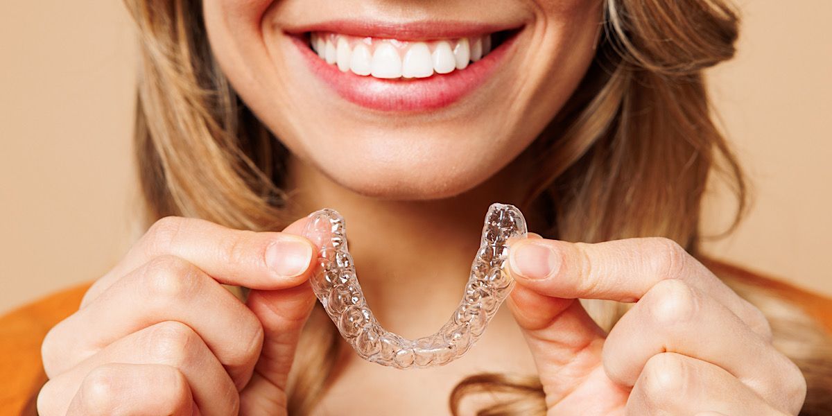 Female showing off her new smile while holding invisalign retainers.