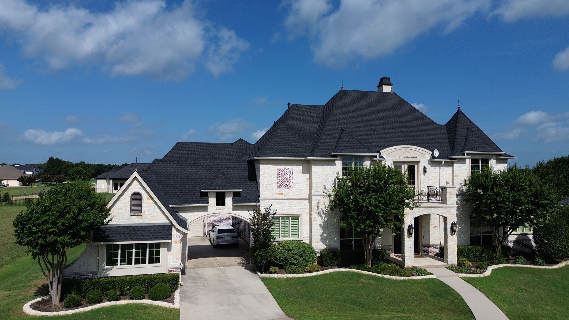 Large white stone house with black roof, green lawn, and blue sky.