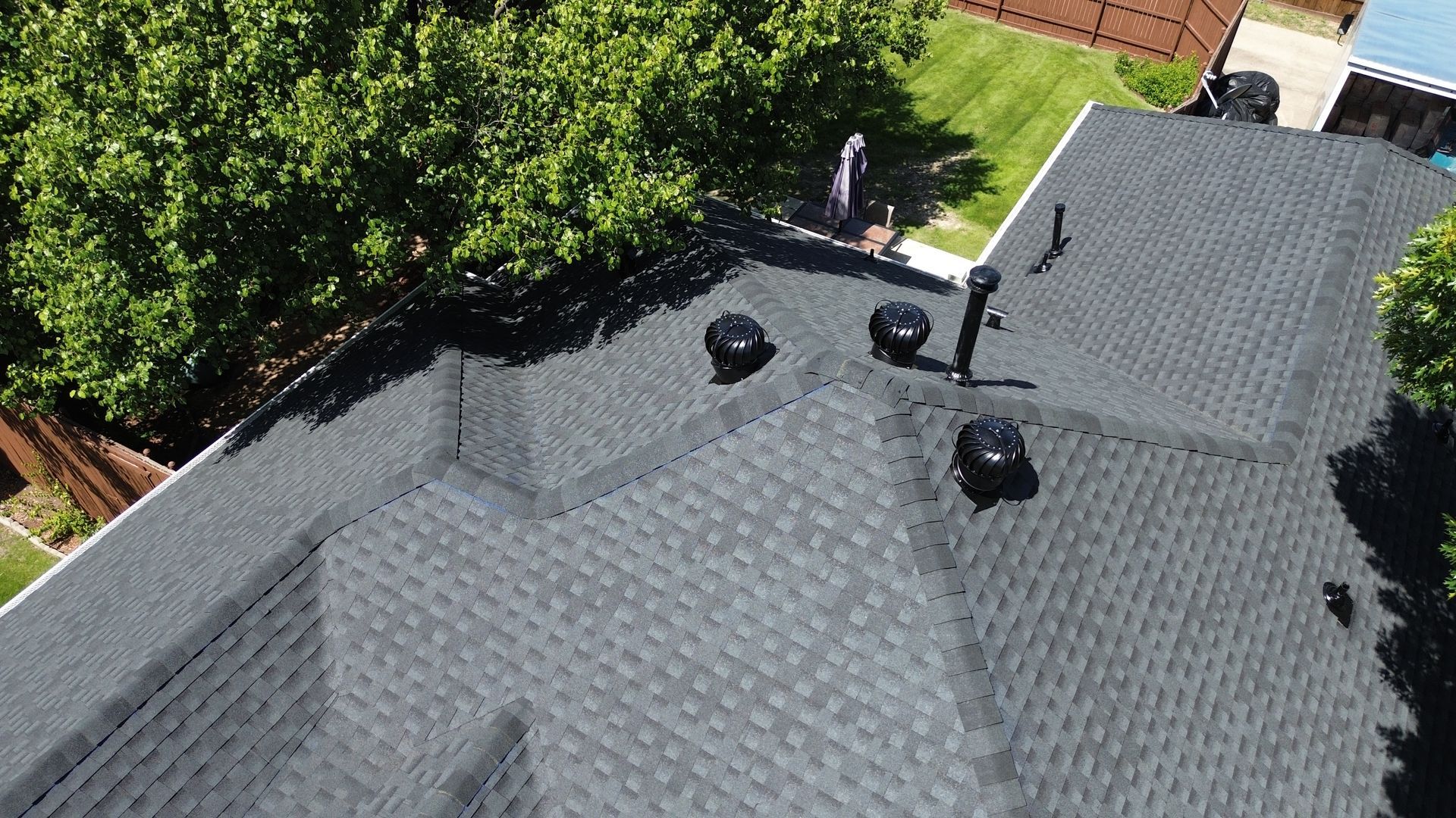 Aerial view of a dark gray shingle roof with three black vent pipes and surrounding greenery.