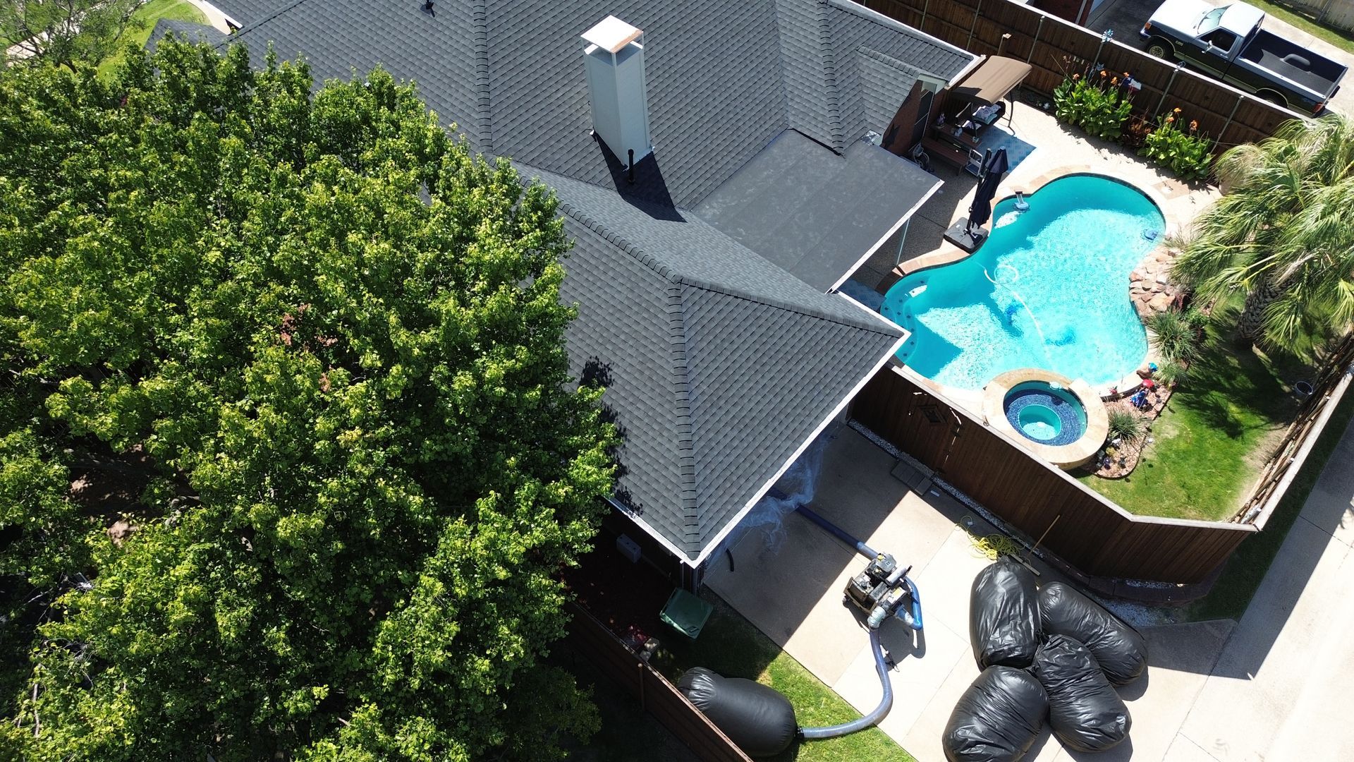 Overhead view of house with black roof, pool, and tree in a yard.