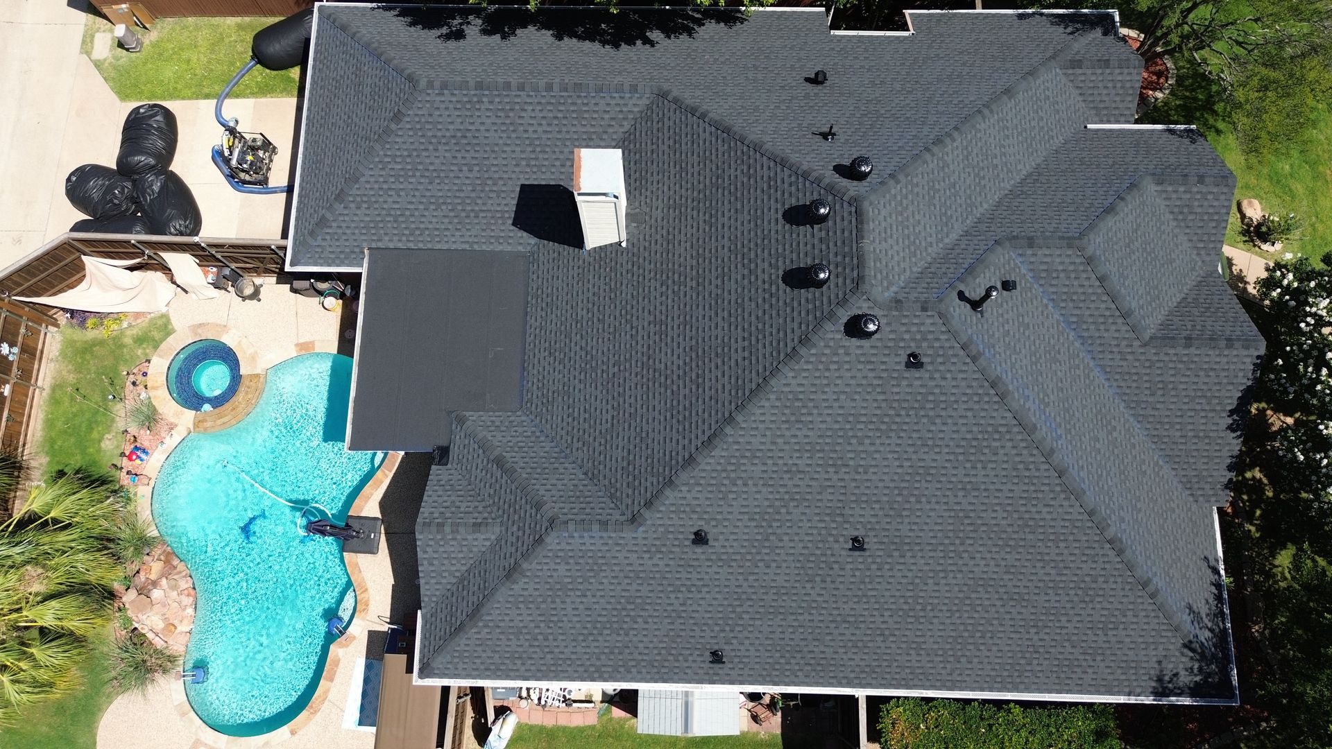 Aerial view of a house with a black shingle roof and a pool.