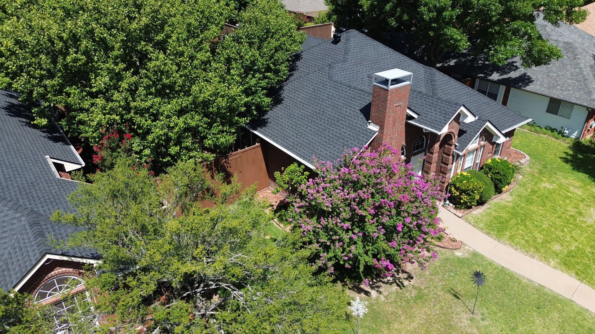 Overhead view of a brick house with a dark roof, surrounded by trees and green grass.