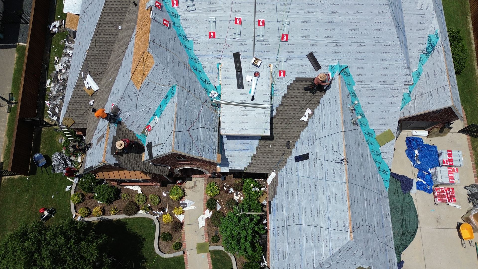 Roofers replacing a roof on a house with green lawn and driveway visible.
