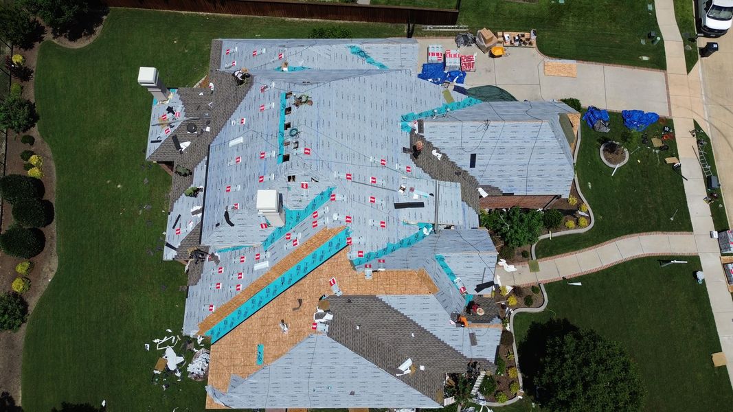Aerial view of a house with roofing shingles being replaced; scattered debris on a lawn and roof.
