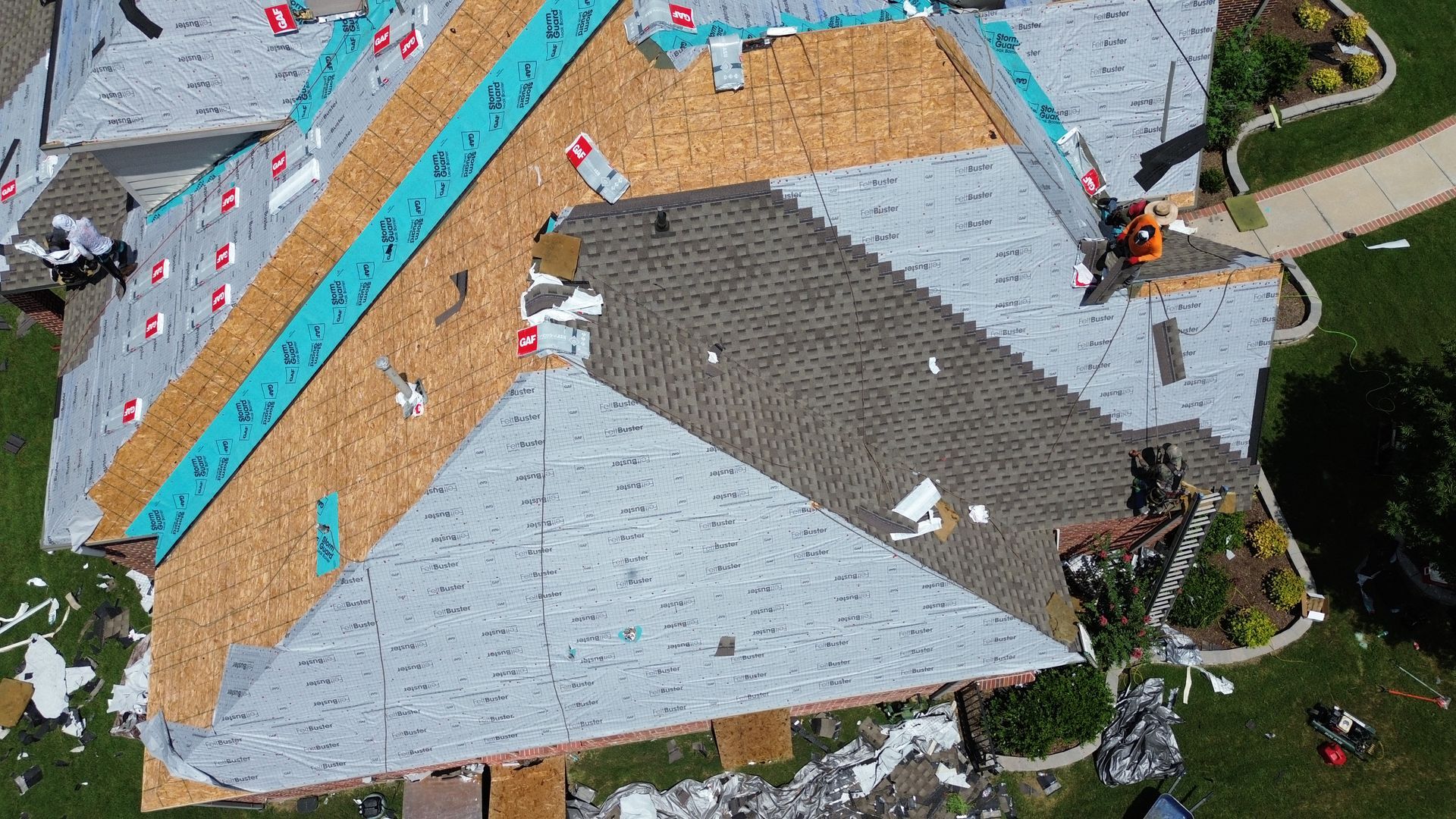 Aerial view of a roof under construction with exposed wood, new shingles, and a worker.