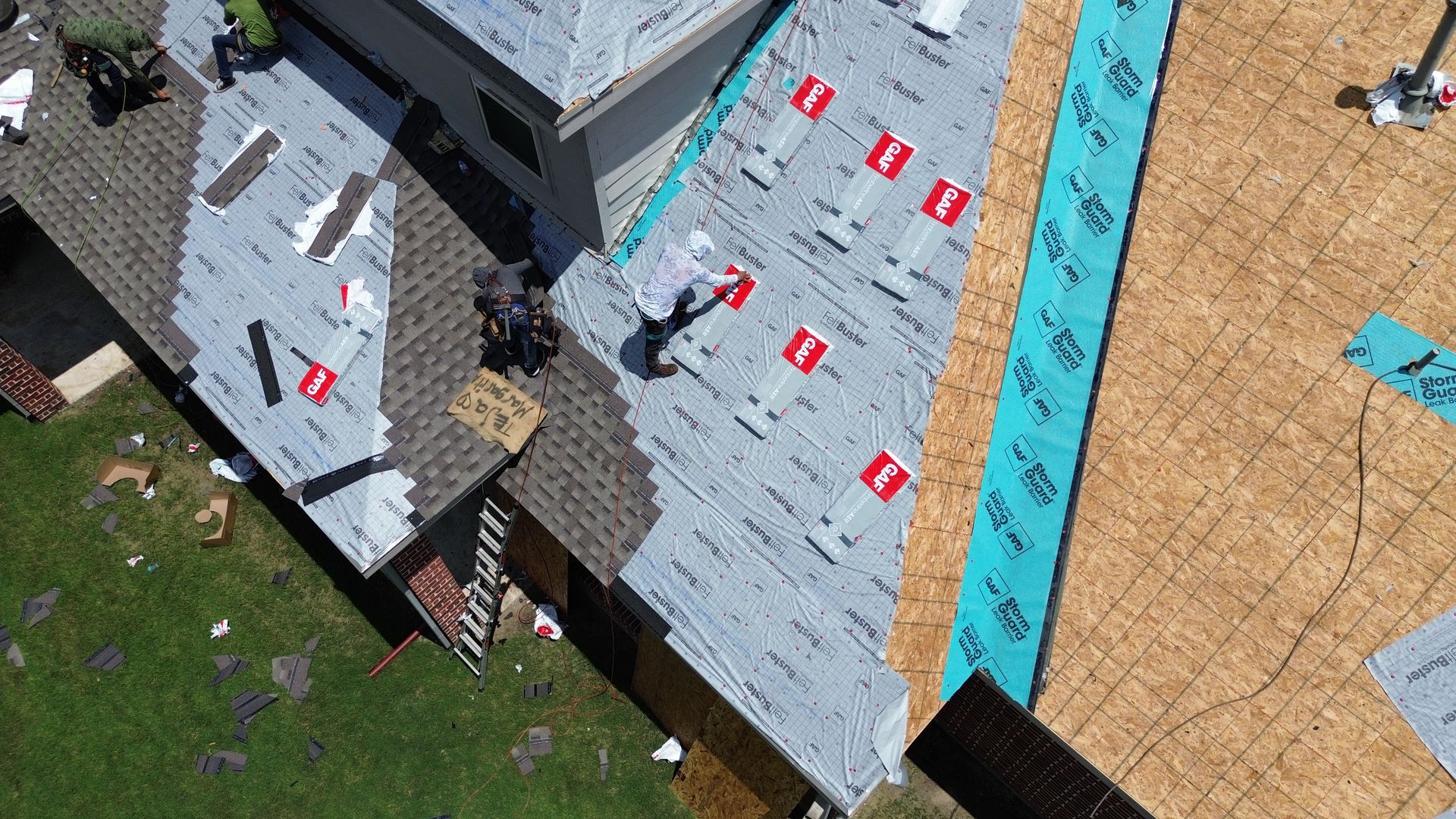 Roofers working on a roof, laying shingles and applying protective underlayment; sunny day.