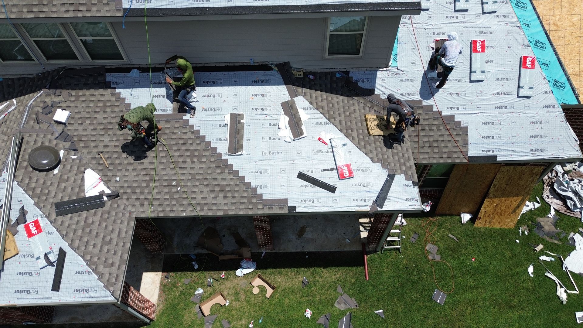Roofers working on a house roof, removing old shingles and installing new ones. Aerial view.