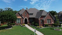 Brick house with a curved walkway, green lawn, and blue sky.