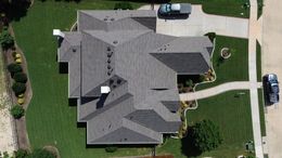 Overhead view of a house with a complex roof, a driveway, lawn, and a car.