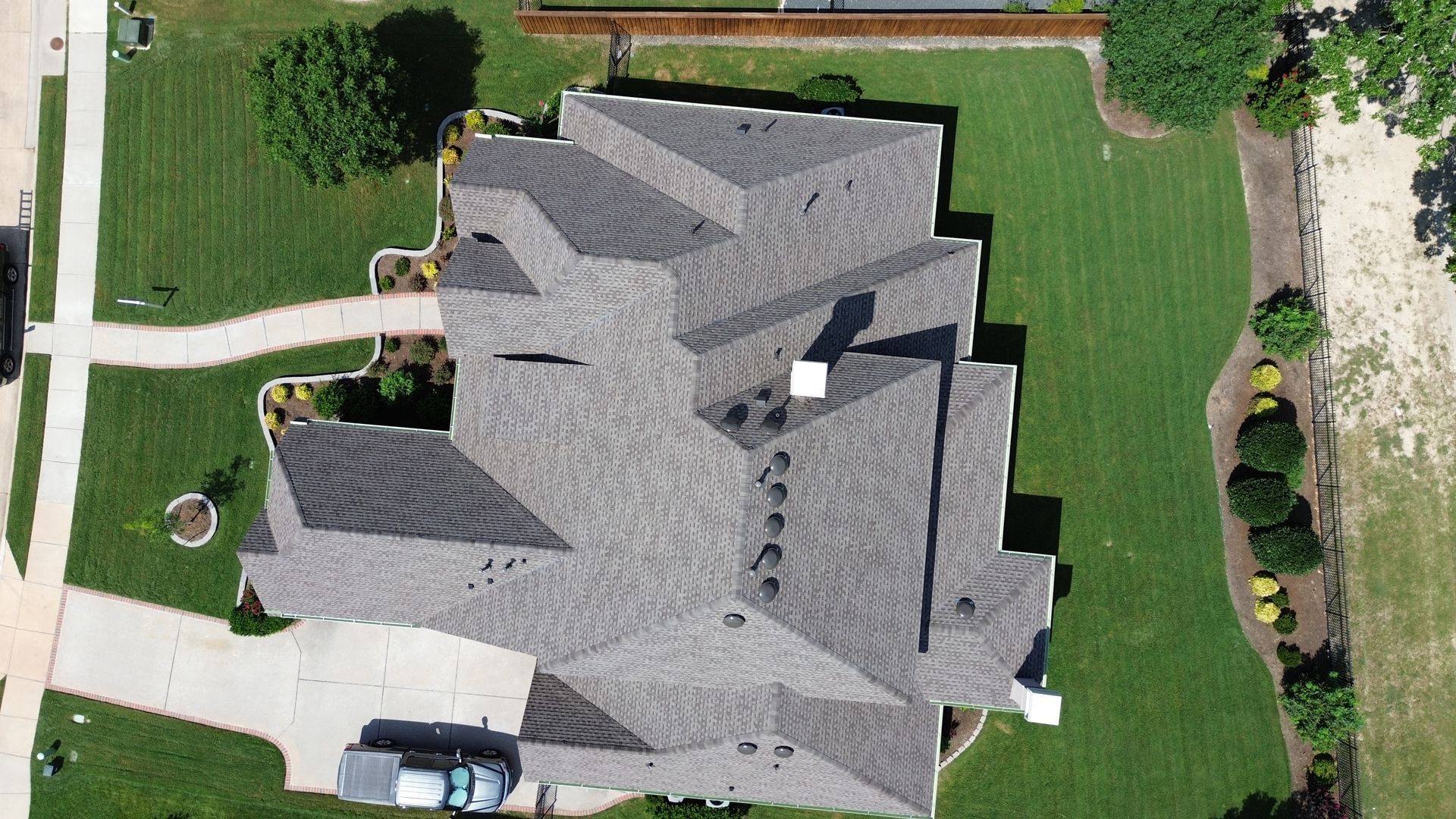 Overhead view of a house with a complex gray roof, surrounded by green lawn and a paved driveway.
