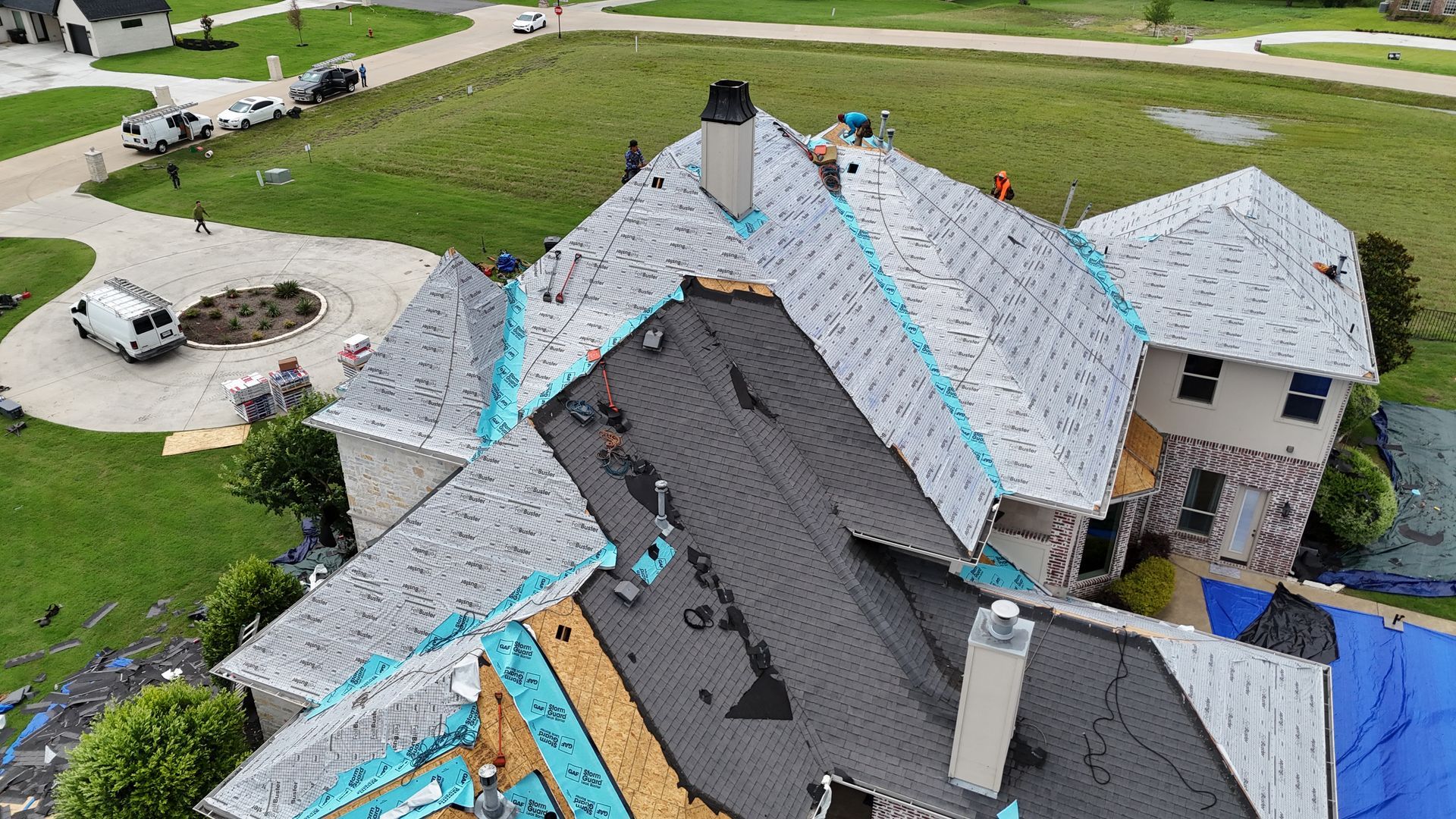 Aerial view of roof construction; workers, tools, and materials on a multi-level gray roof.