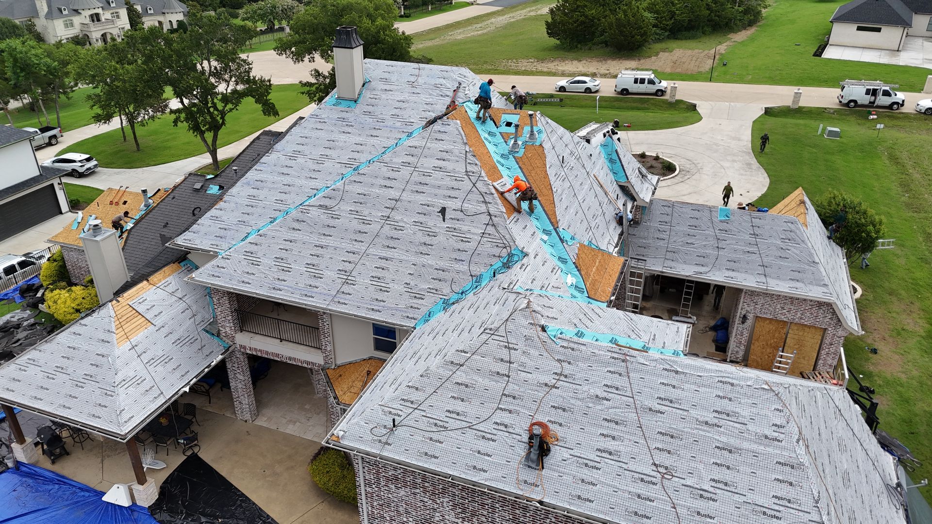 Roofers working on a multi-sectioned house roof, tearing off old shingles and laying new ones.
