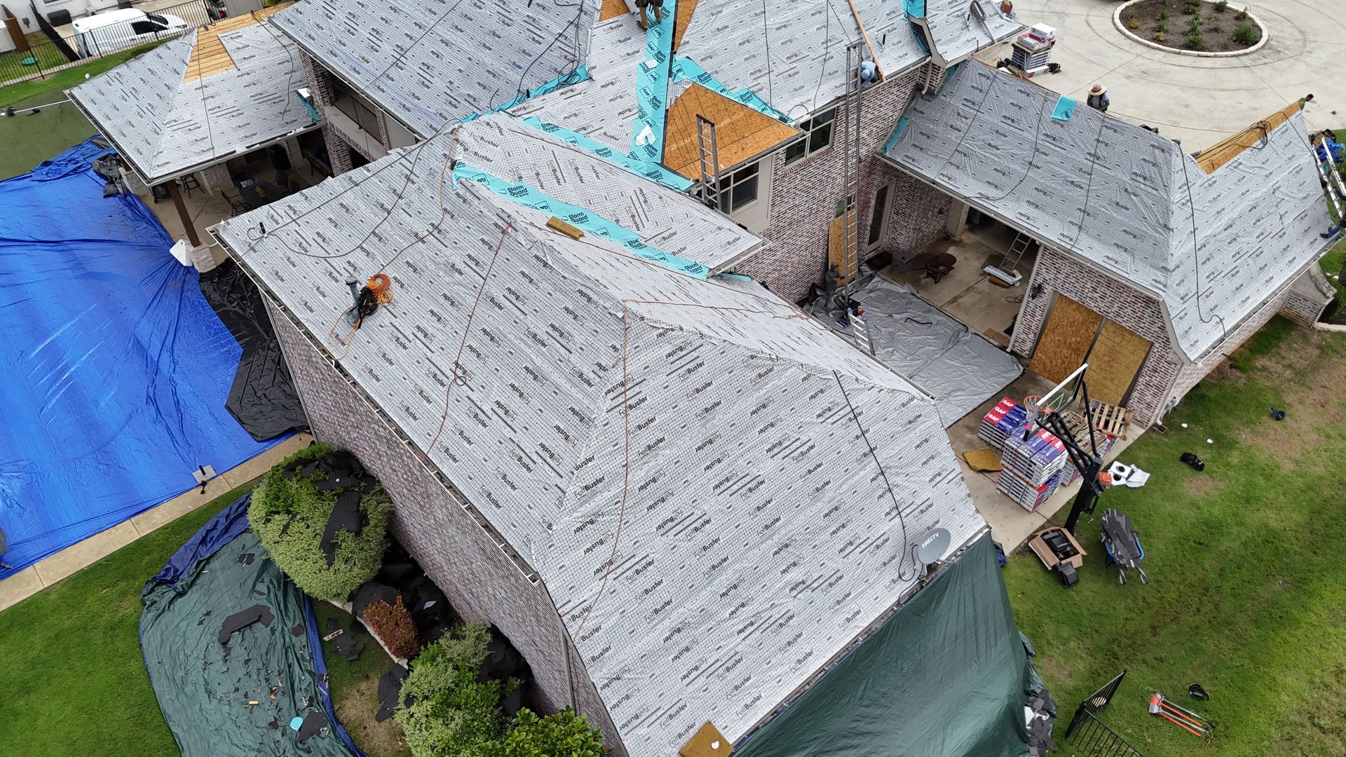 House under construction; roof with new shingles and tarps, workers visible.