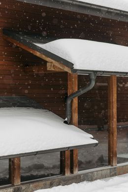 Snow-covered wooden structure with a gutter and downspout; it's snowing.