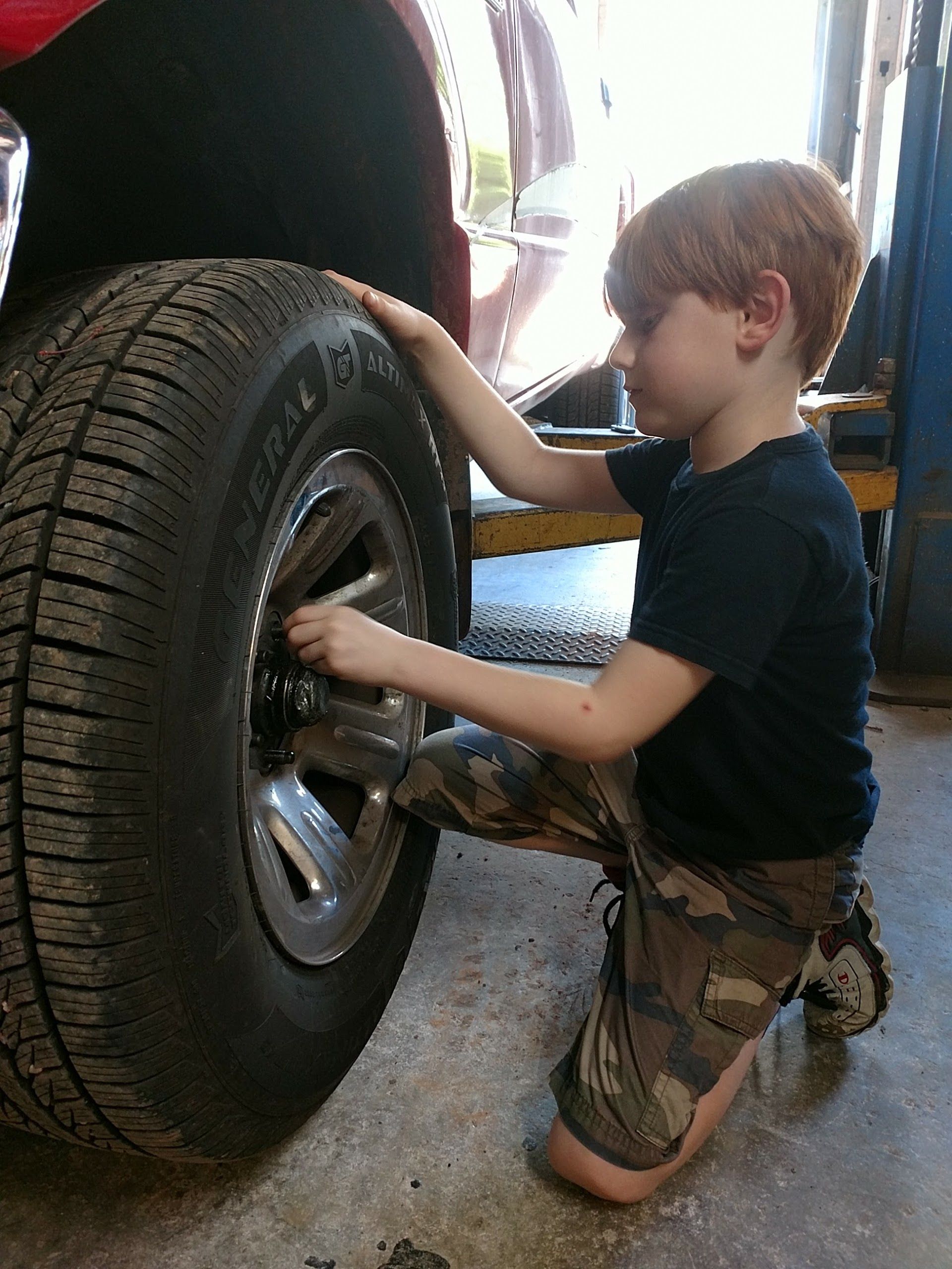 Young boy kneeling, working on a car tire in a garage. He's using a wrench. | Rock's Tire & Auto