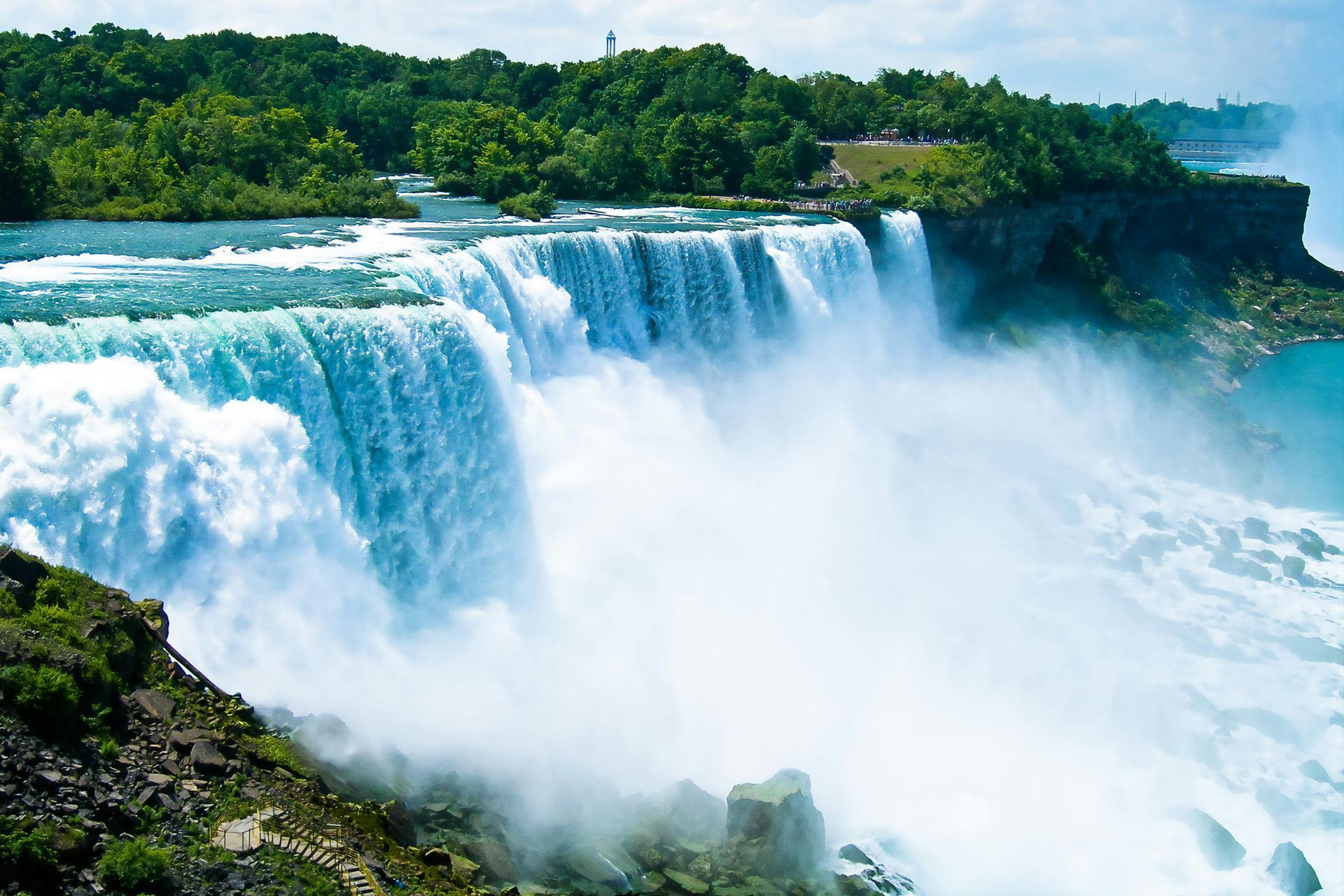Wide waterfall plunging into mist amid lush green cliffs and trees