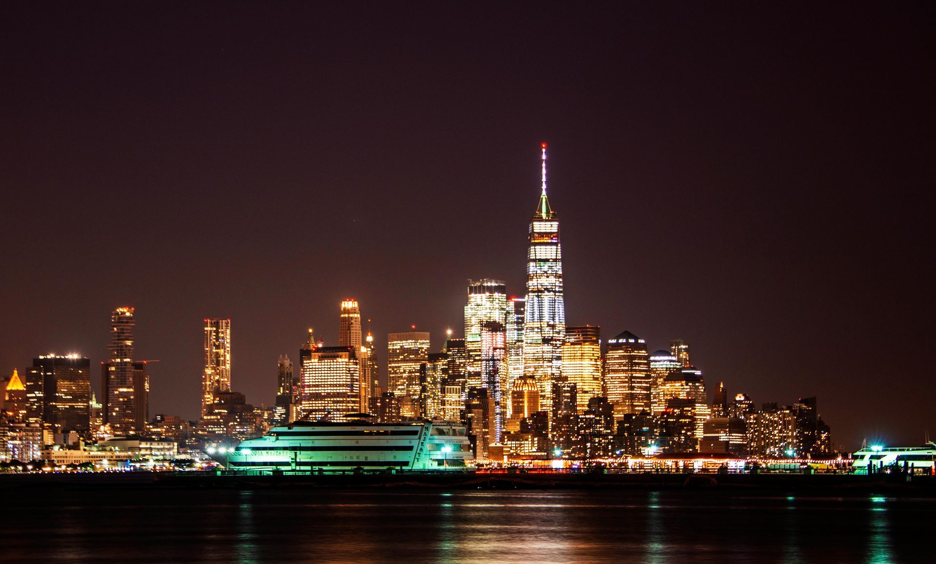 Nighttime skyline with a lit skyscraper and waterfront reflections.
