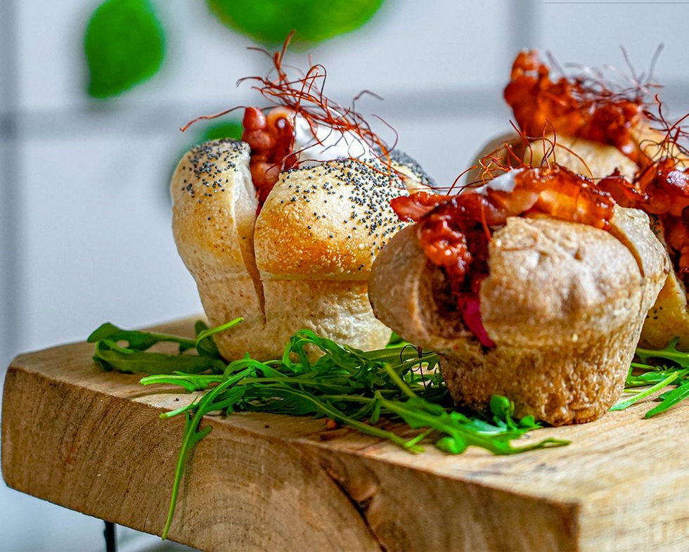 Mini ciotole di pane salato riempite di cibo, guarnite con verdure, disposte su un tagliere di legno.