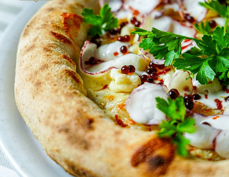 Pizza con polpo, formaggio bianco e guarnizione di prezzemolo su un piatto bianco.