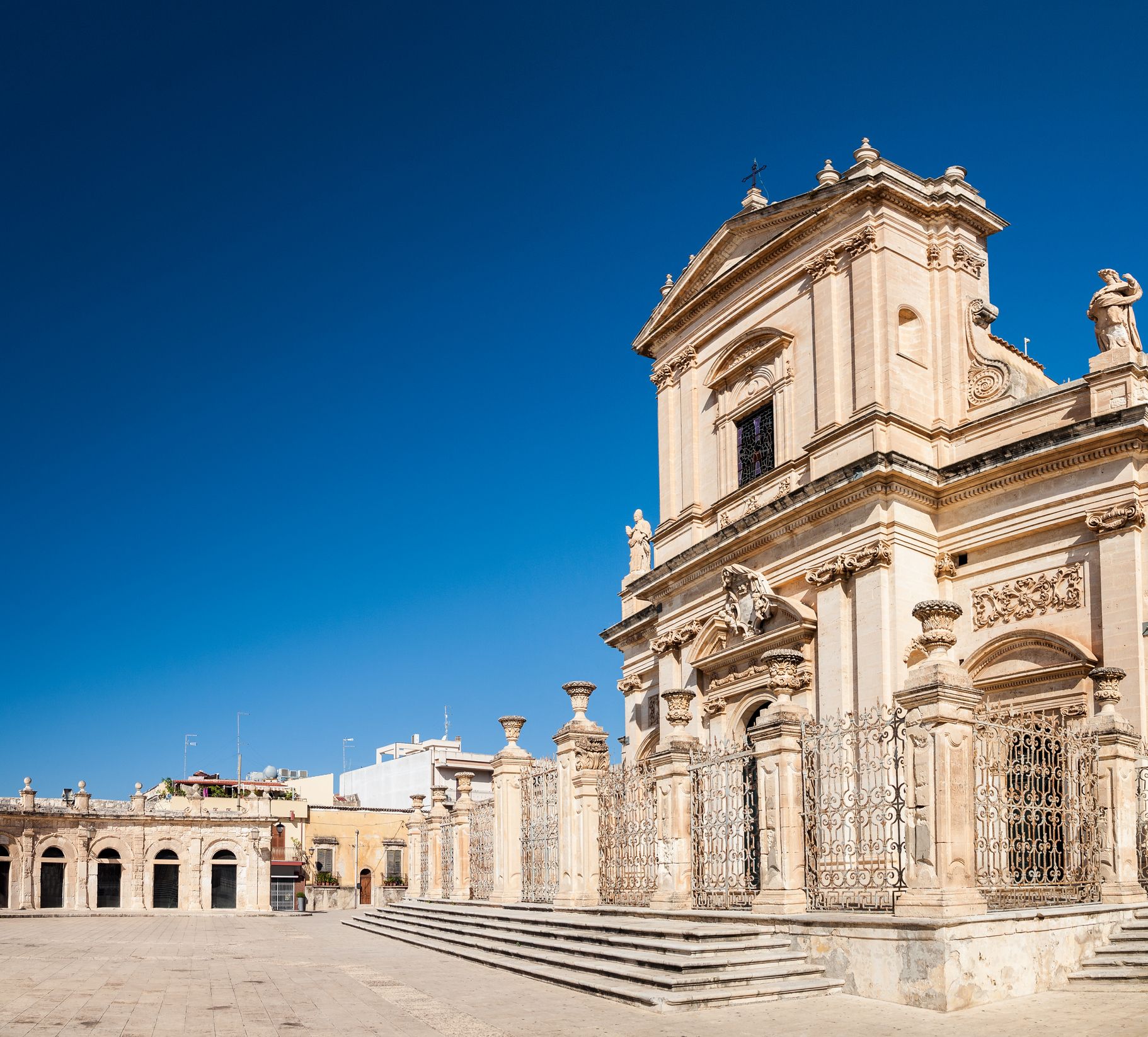 Facciata di una chiesa barocca contro un cielo azzurro terso; scale e un cancello decorativo di fronte.