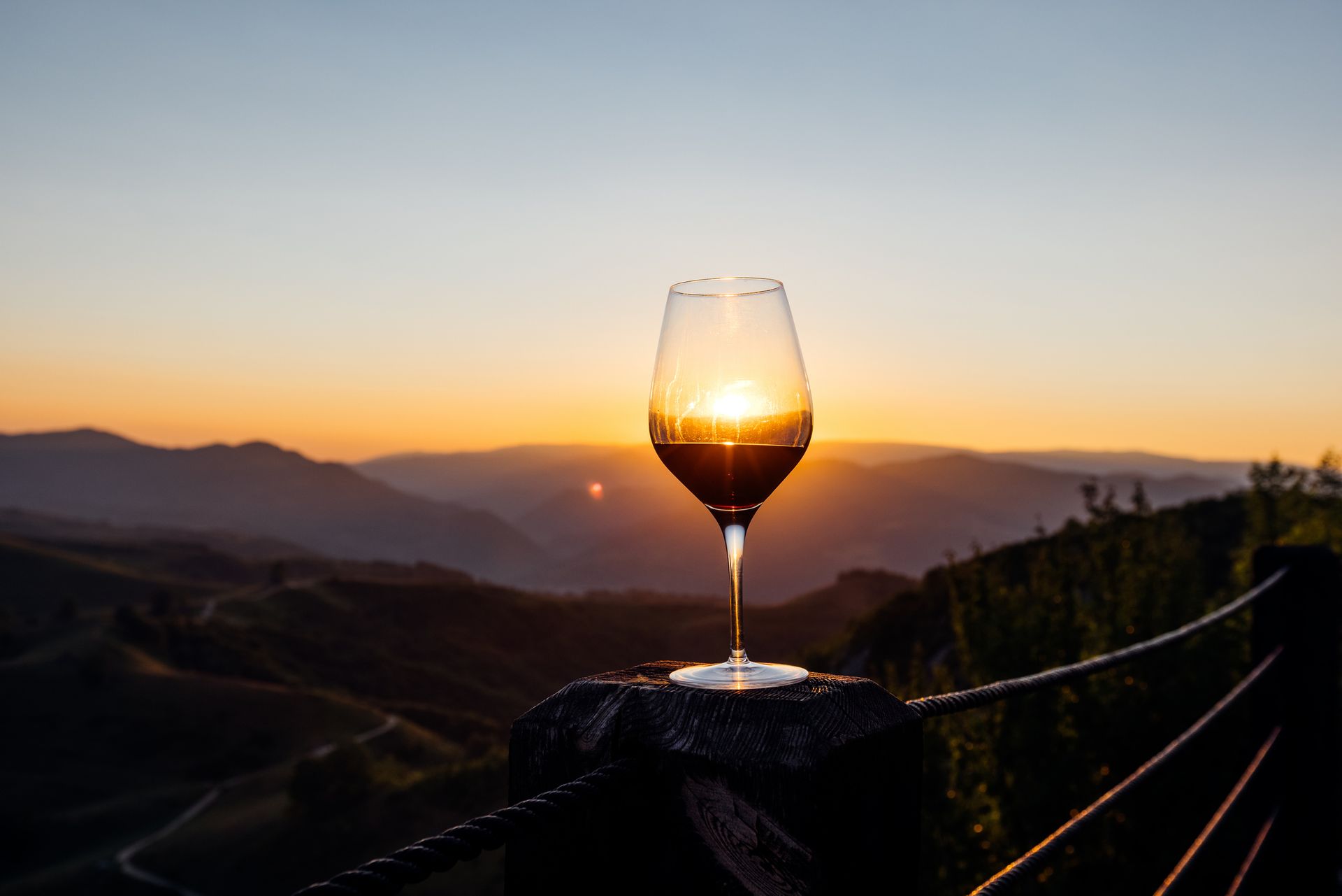 Bicchiere di vino rosso, sole che tramonta dietro le montagne.