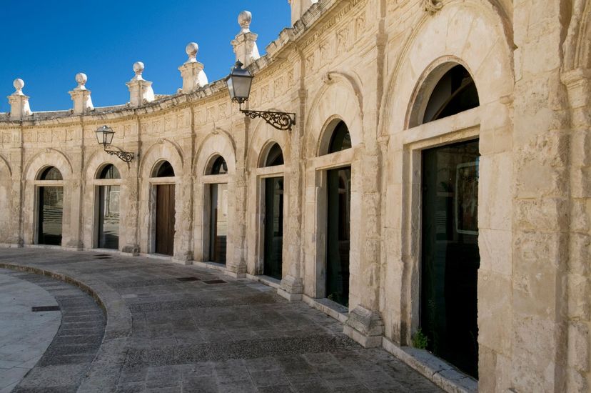 Corridoio con archi in pietra e porte scure sotto un cielo azzurro brillante.