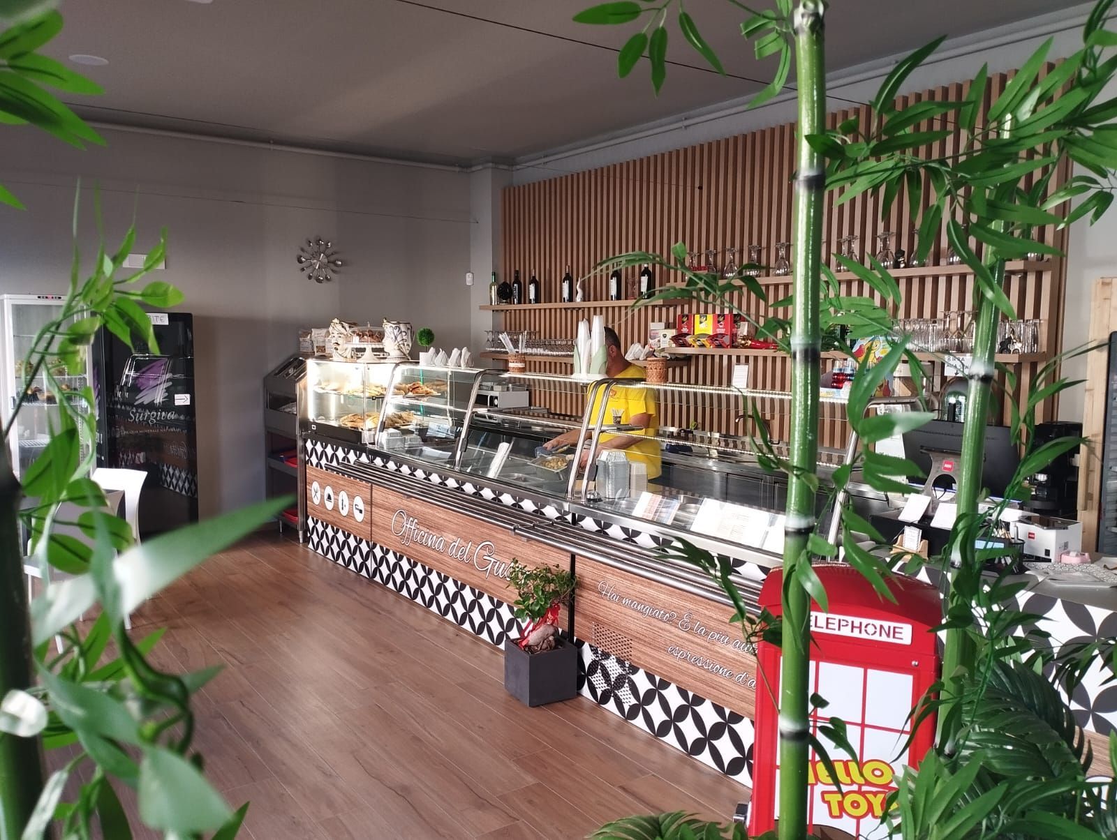 Interno di un bar con un bancone che espone cibo, elementi in bambù e un giocattolo rosso.