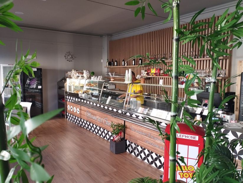 Interno di un bar con bancone espositivo, elementi in legno e piante decorative di bambù.