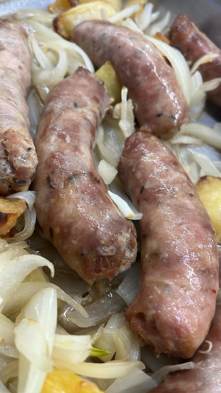 Salsicce cotte in padella con cipolle e patate, primo piano.