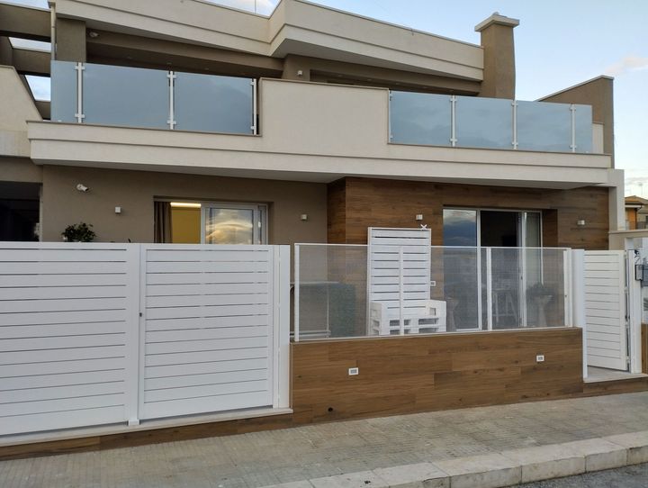 Casa moderna a due piani con recinzione bianca e balconi in vetro.