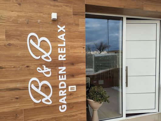 Cartello per B&B Garden Relax su una parete rivestita in legno accanto a una porta bianca e una finestra in vetro.