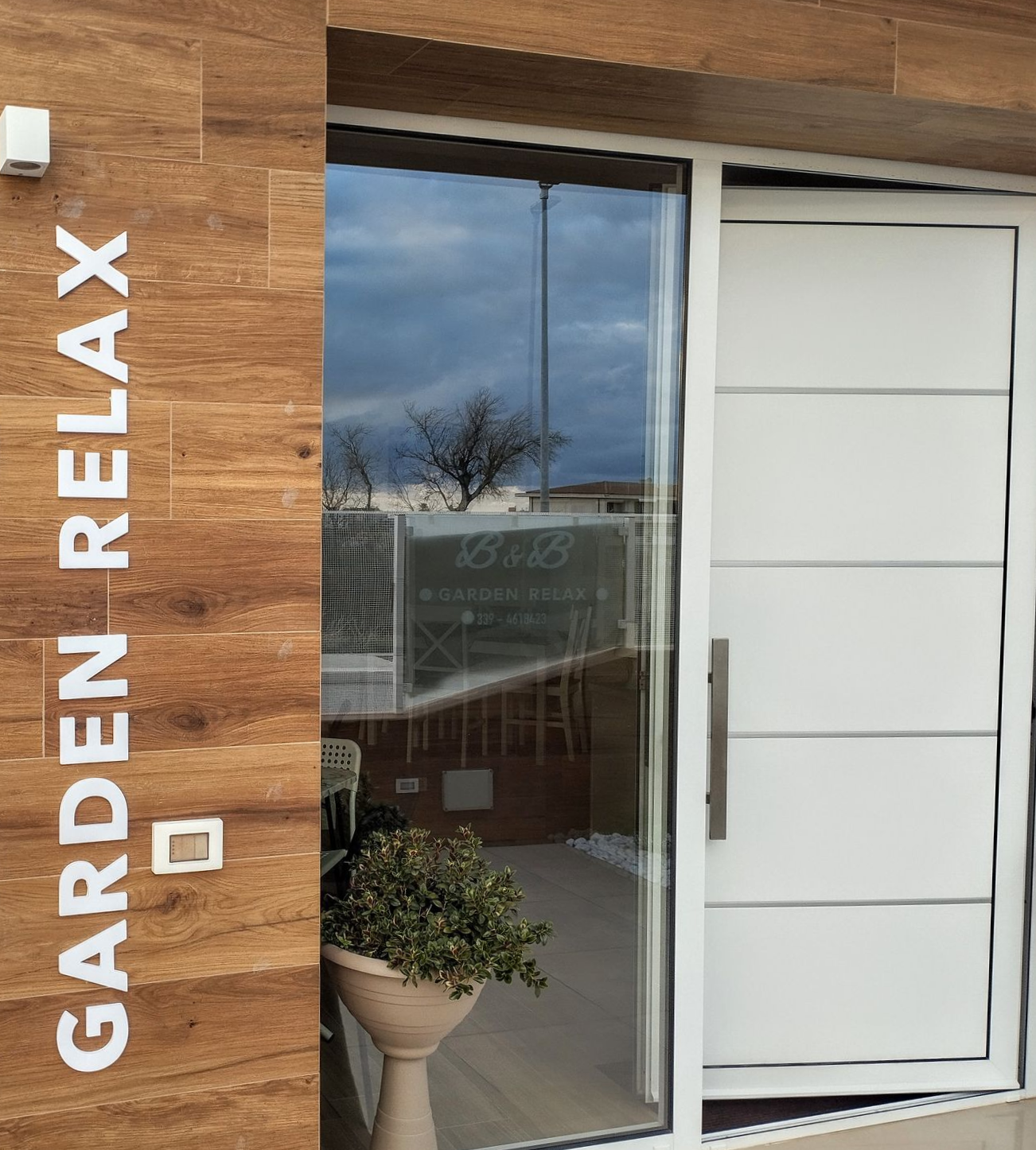 Cartello per B&B Garden Relax su una parete rivestita in legno accanto a una porta bianca e una finestra in vetro.