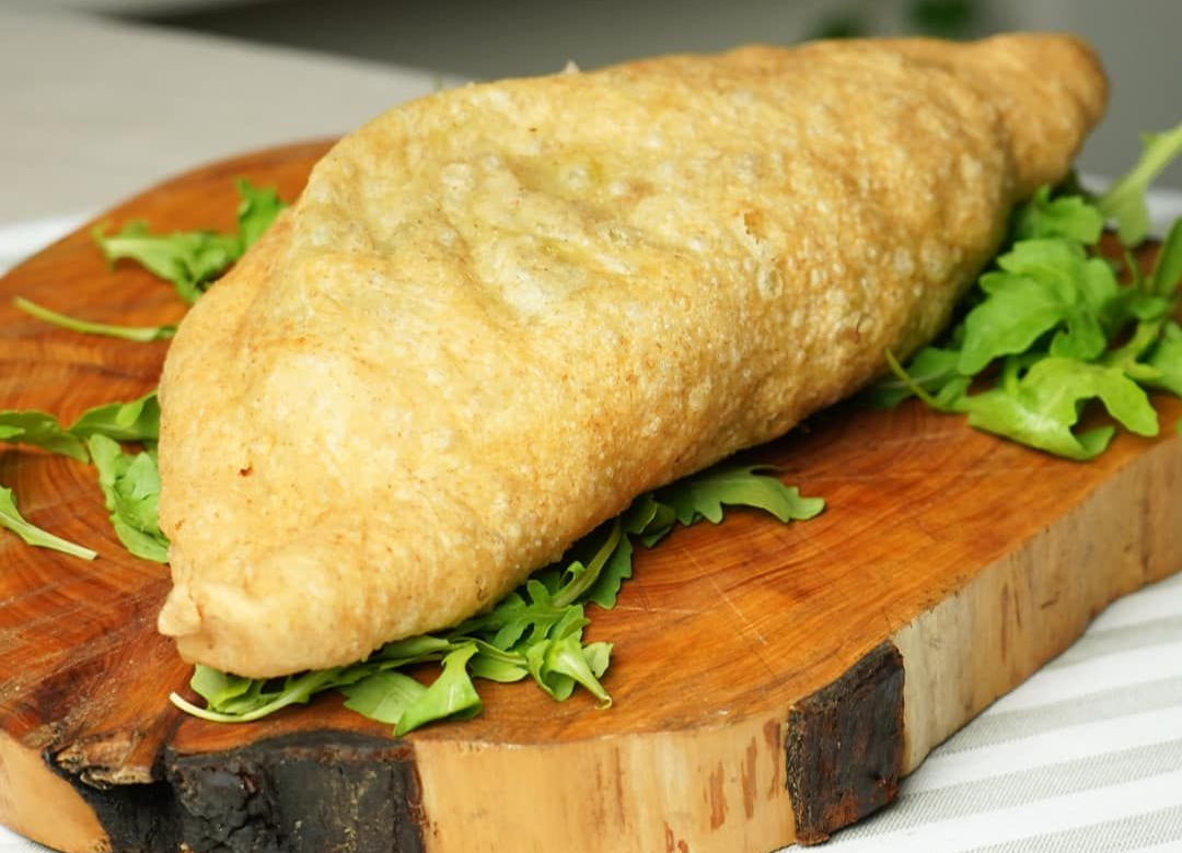 Calzone fritto su un tagliere di legno con guarnizione di foglie verdi.