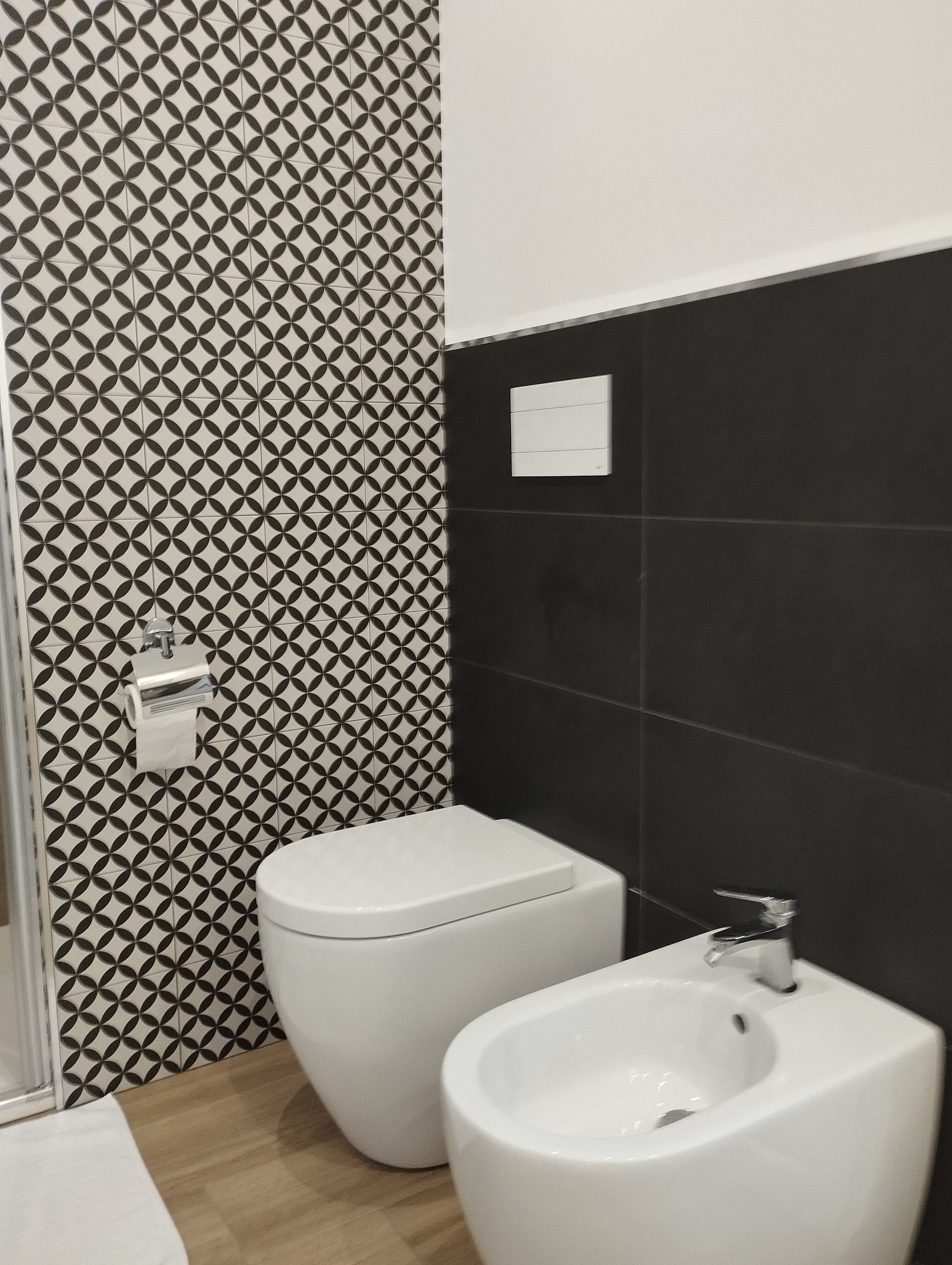 Bagno con WC e bidet bianchi, parete piastrellata con motivi bianchi e neri e parete piastrellata con motivi neri.