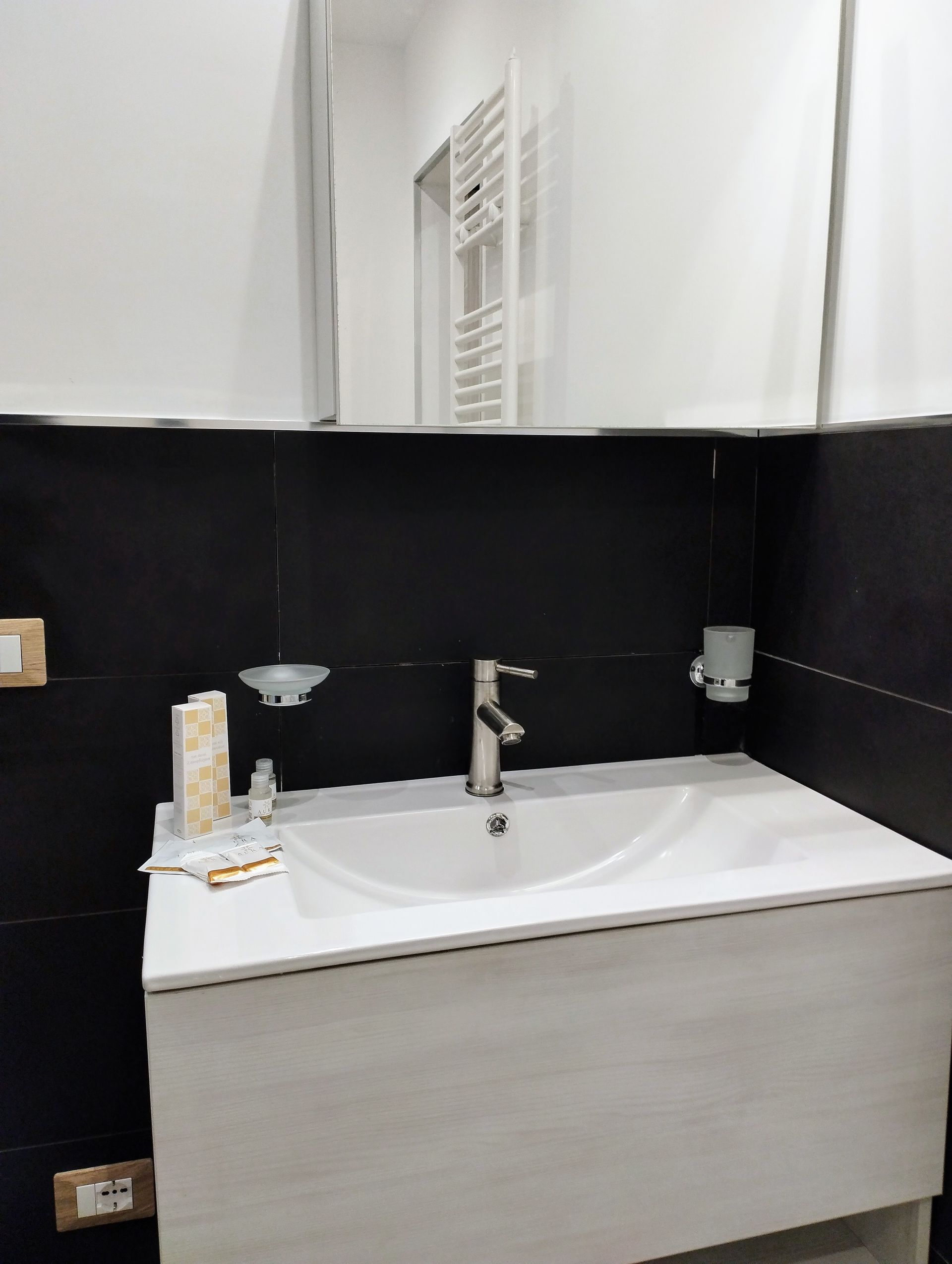 Lavandino del bagno con lavabo in porcellana bianca, rubinetto cromato, parete nera e un grande specchio.