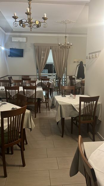 Sala da pranzo con sedie e tavoli in legno, tovaglie bianche e lampadari.