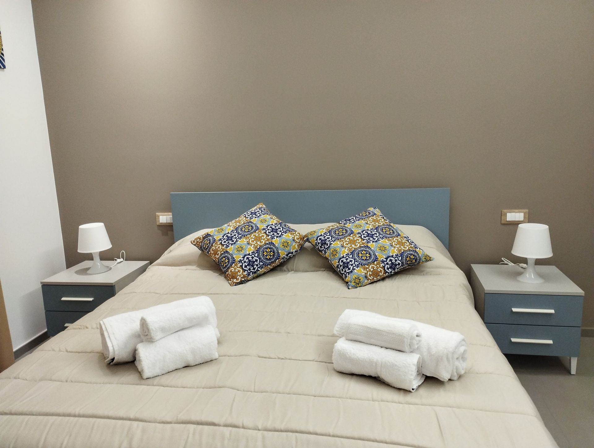 Camera da letto con letto matrimoniale, due comodini con lampade, asciugamani piegati sul letto.