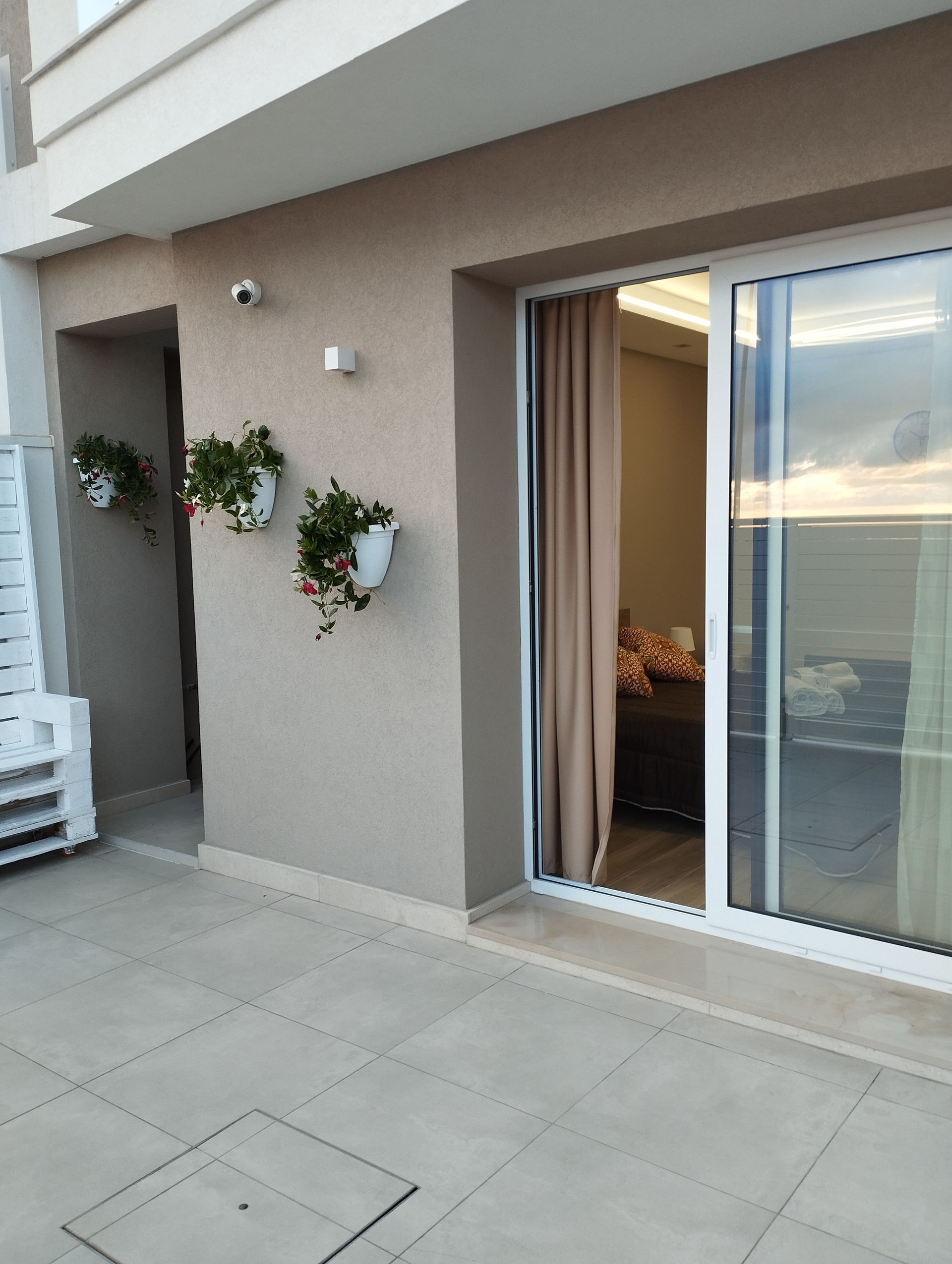 Balcone con porta scorrevole in vetro, fiori, pareti beige e tende color cuoio.
