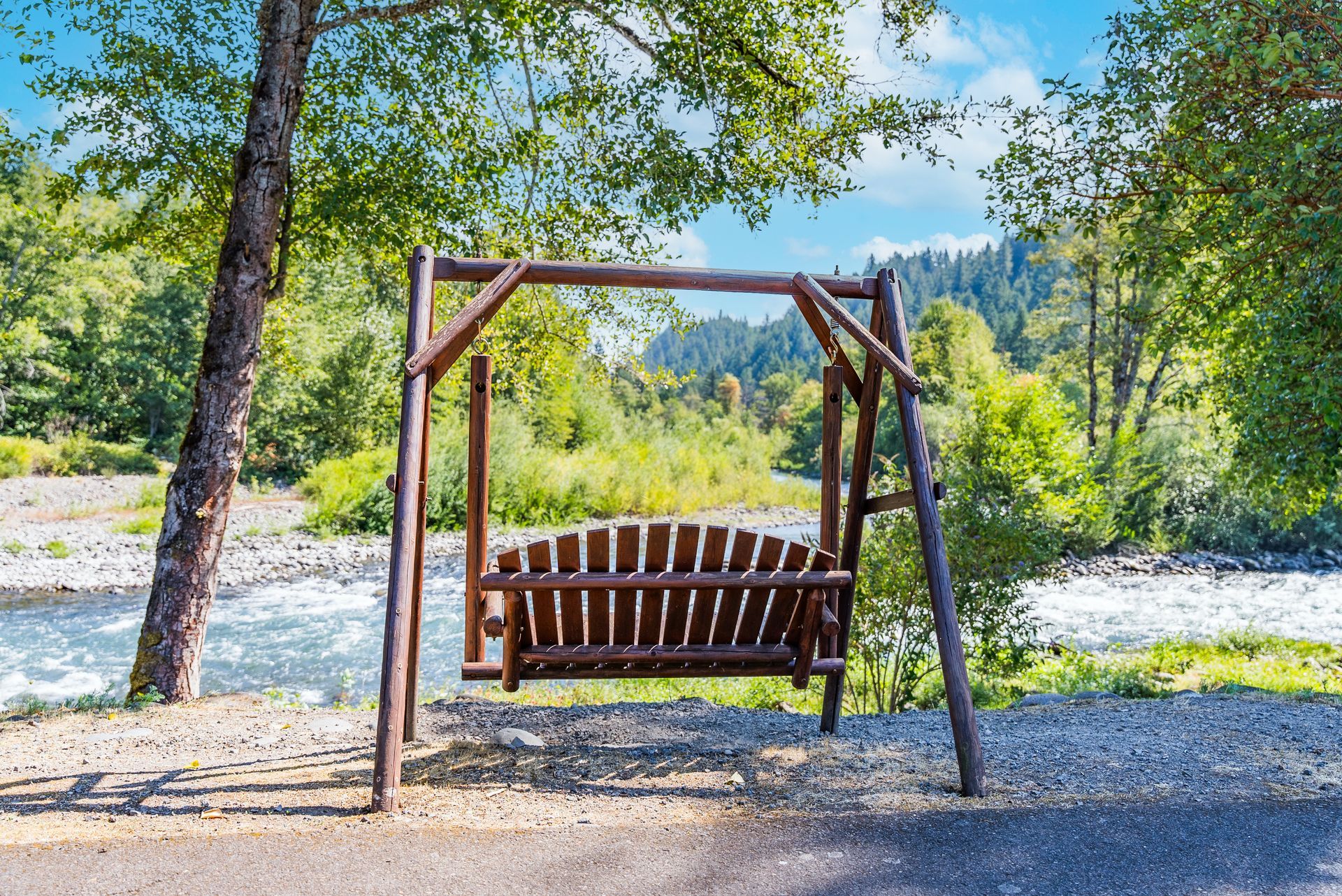Wooden swing seat overlooking a river and green forest under a blue sky.
