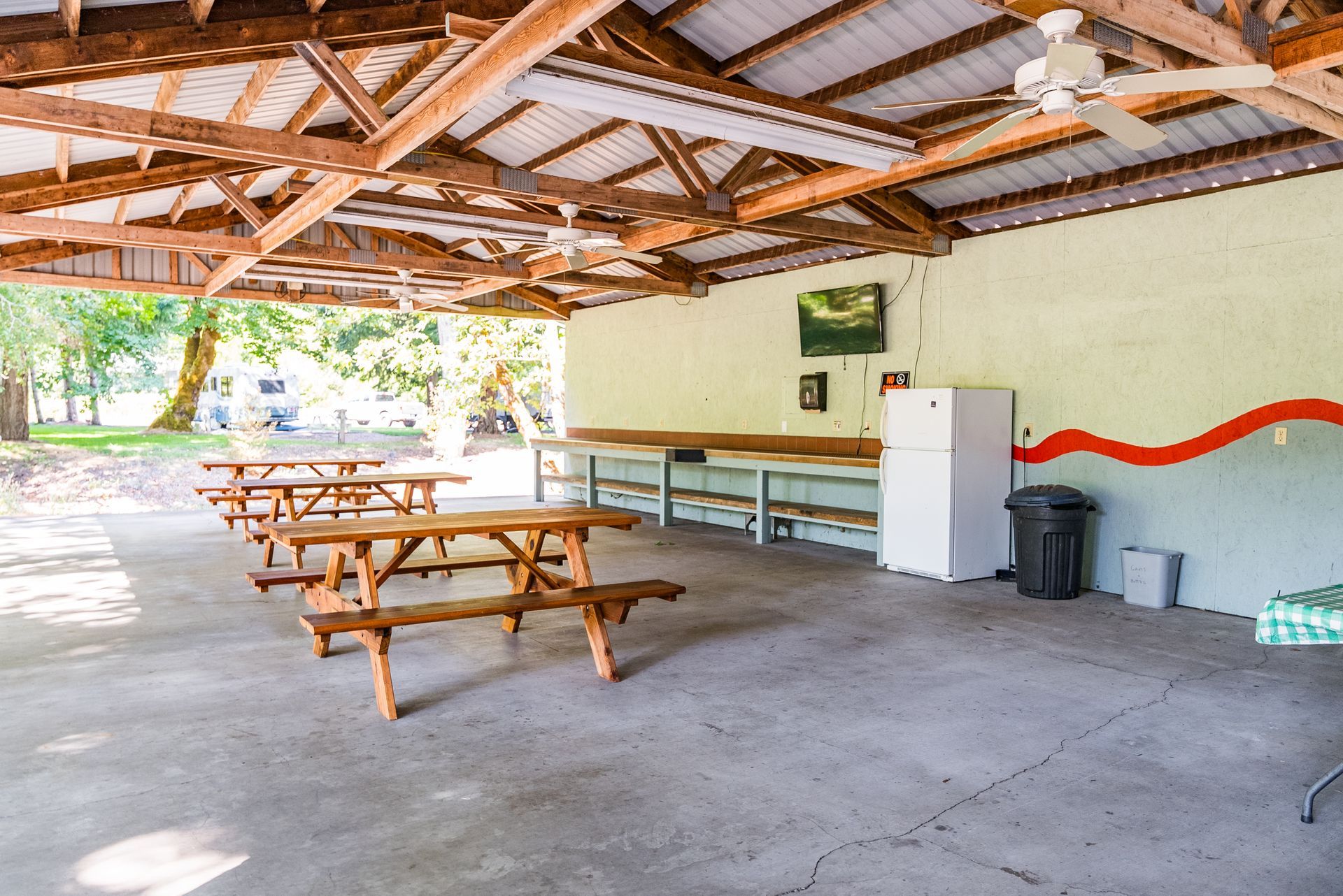 Picnic shelter with wooden tables, concrete floor, and white refrigerator.