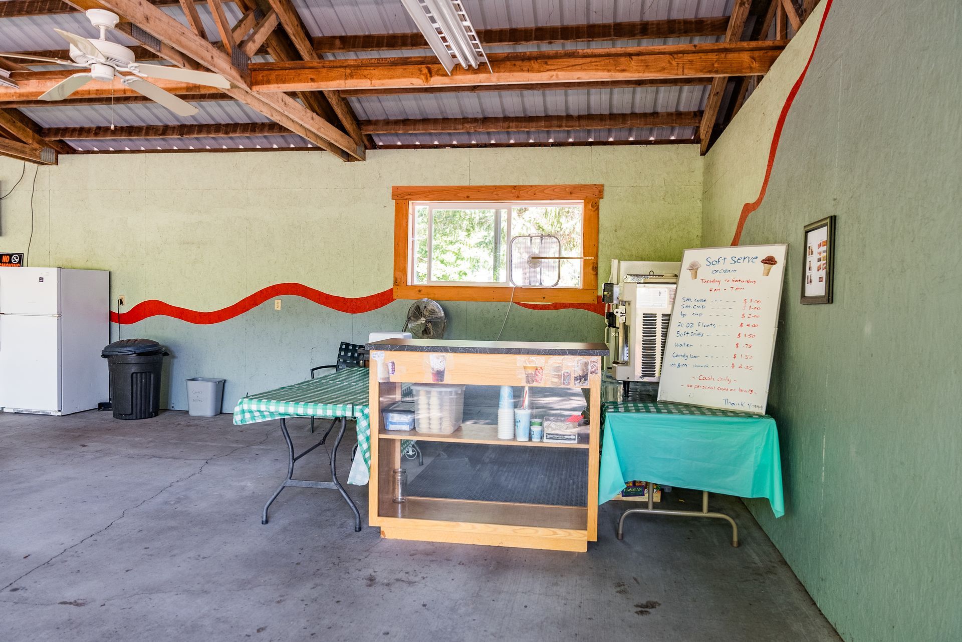 Indoor space with concrete floor, fridge, tables, window, and supplies.