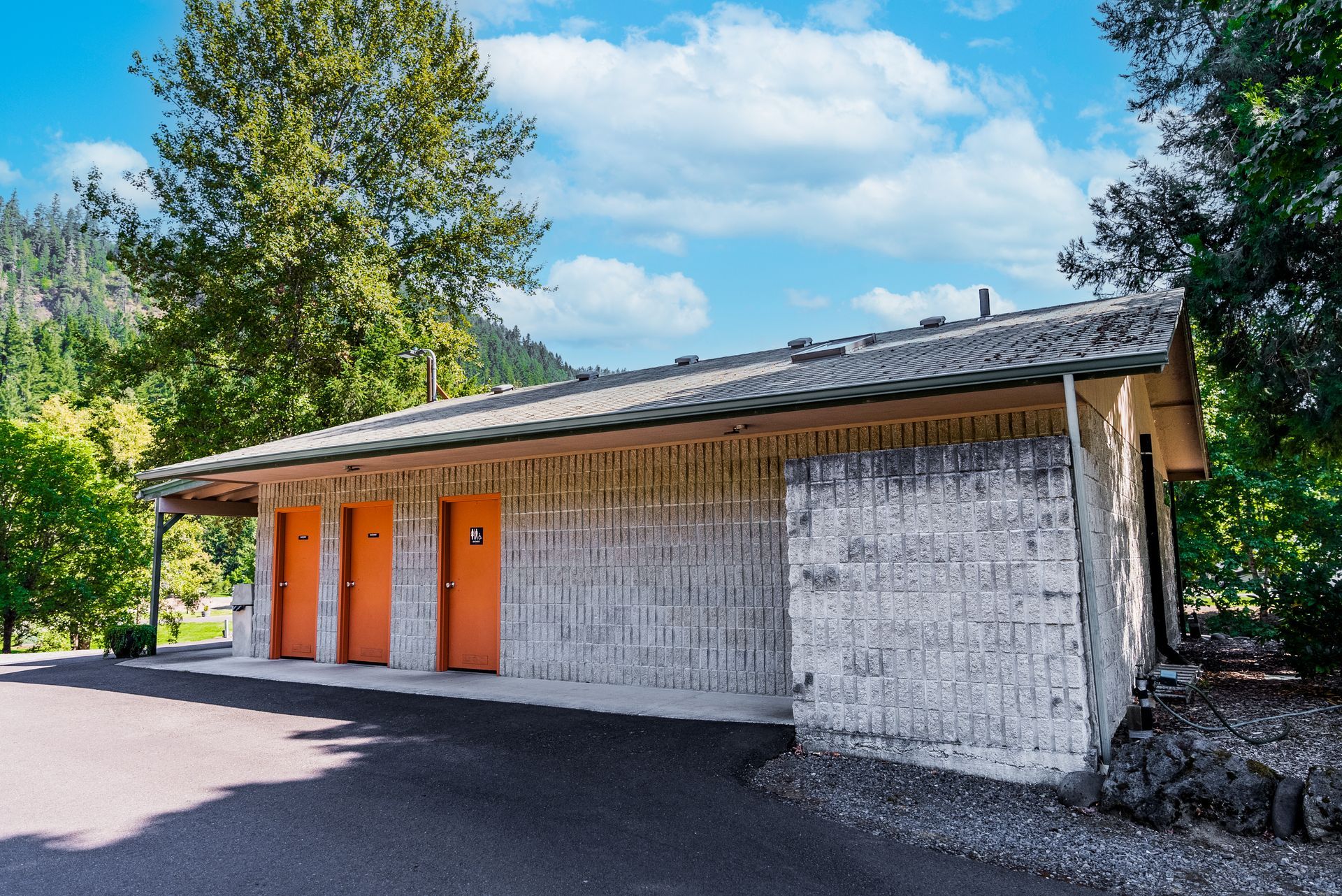 Public restroom building with orange doors. Exterior has white, textured siding and a sloped roof.
