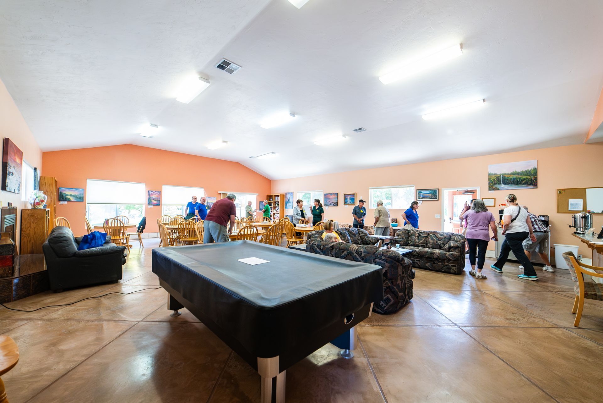 People in a community center playing pool and socializing. Interior with couches, tables, and art.